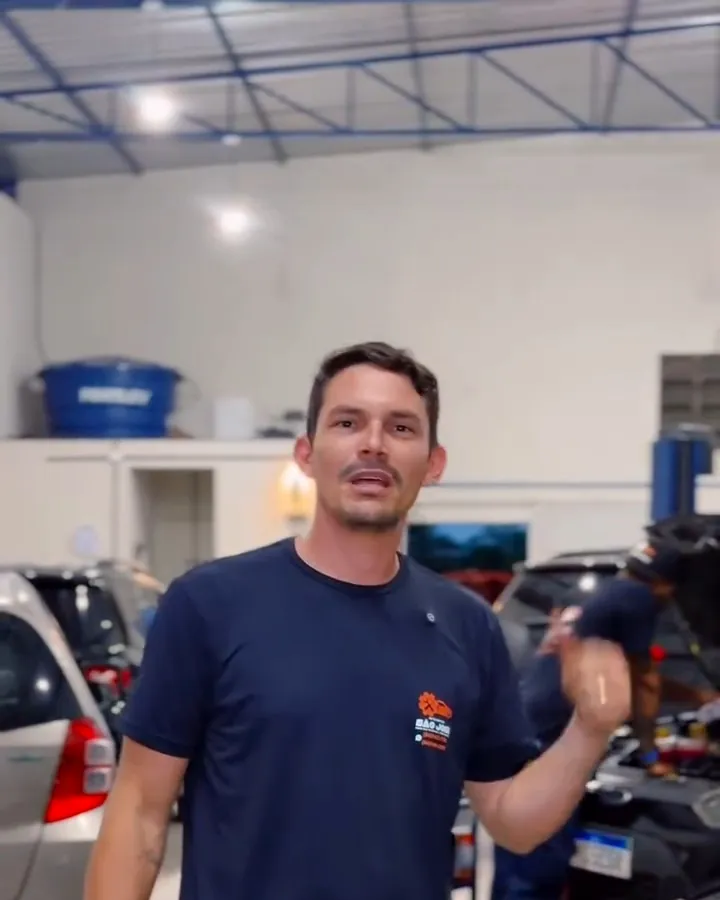 Mecânico conversando dentro da oficina com carros ao fundo